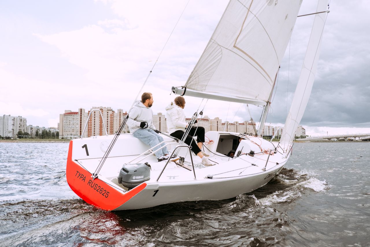 Two people sailing on a yacht near city buildings, enjoying a nautical adventure.
